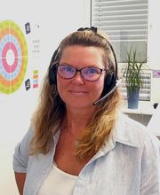 Eine Frau mit Brille und langen blonden Haaren. Sie trägt ein Headset auf dem Kopf.