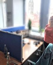 Teilnehmerin steht am Arbeitsplatz am Fenster