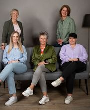 Eine Gruppe von 5 Frauen, die teilweise stehen und teilweise auf einer Couch sitzen.