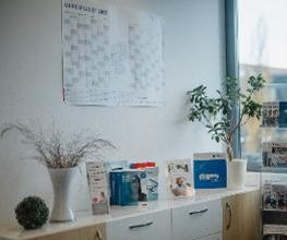 Regal mit Flyern und Büchern. Darüber ein Jahres-Wandkalender.