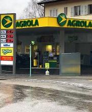 AGROLA Tankstelle in Liebefeld mit TopShop; regnerische Aufnahme; Tankstelle bei Kreisel gelegen; links Totem mit AGROLA Logo, digitaler Preisanzeige, AdBlue und TopShop Logo darunter