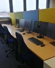 Mehrere PC-Arbeitsplätze mit Monitoren, Tastatur, Maus und Headset.