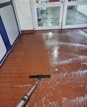 E&E Gebäudereinigung Gründliche Bodenreinigung eines roten Fliesenbodens, bei der Schmutz und Reinigungsrückstände mit einem Absauggerät entfernt werden, um eine saubere und gepflegte Oberfläche zu erzielen.