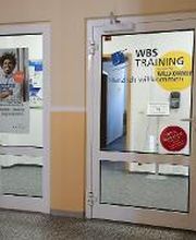 Eingangsbereich mit zwei Glastüren. Auf der Linken ist ein WBS-Poster aufgeklebt, auf der rechten steht "WBS TRAINING. Herzlich willkommen"
