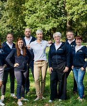 Mehrere Frauen und Männer posieren auf einer Wiese für ein Gruppenfoto.