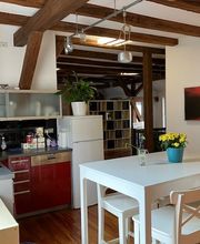 Küche mit Schränken, Kaffeemaschine, hohem Tisch und vier erhöhten Stühlen. 