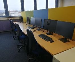 Mehrere PC-Arbeitsplätze mit Monitoren, Tastatur, Maus und Headset.