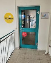 Türkise Eingangstüre im Hausflur. Glastüre mit WBS TRAINING Aufkleber und blauem Logo. Daneben ein gelbes Wandtattoo mit der Aufschrift „Herzlich Willkommen.“