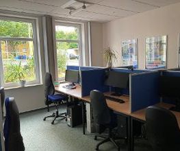 Drei voneinander abgegrenzte Arbeitsplätze nebeneinander mit Bildschirmen, Stuhl und Tastatur. An der Wand mehrere Plakate der WBS TRAINING.