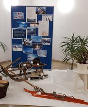 Winter-Dekoration im Foyer. Ein Schlitten, Skier und ein Hockeyschläger auf einem weißen Teppich. Dahinter ein Aufsteller mit verschiedenen Fotos und einigen Zimmerpflanzen. An der Wand hängt ein gelber Aufkleber mit der Aufschrift Herzlich Willkommen.