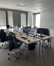 Ein Schulungsraum mit mehreren Arbeitsbereichen. Jeder Arbeitsplatz besteht aus 2 PC-Bildschirmen, Tastatur und Maus sowie Headset.