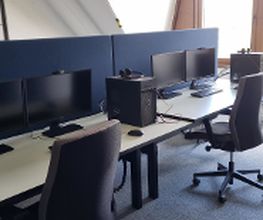 Ein Schulungsraum mit mehreren Arbeitsbereichen, die durch blaue Trennwände voneinander getrennt sind. Jeder Arbeitsplatz besteht aus 2 PC-Bildschirmen, Tastatur und Maus sowie Headset und blauen Trennwänden.