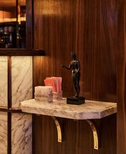 A wall-mounted marble shelf holding a dark bronze female figurine and holders with pink napkins against a warm, dark wood paneled backdrop.