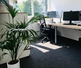 Schreibtisch im Trainingsraum mit zwei Bildschirmen, Tastatur, Headset und Maus. Durch das Fenster strahlt viel Sonnenlicht herein.