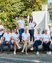 Mehrere Personen in weißen WBS TRAINING Poloshirts sitzen und stehen auf einem Brunnenrand.