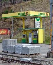 AGROLA Tankstelle in Mogelsberg; Im Vordergrund Zuggleise und Paletten mit Setzsteinen. AGROLA Tankstelle mit zwei Säulen und Zahlterminal. Totem mit Preisen im Hintergrund