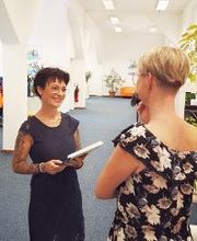 Zwei Frauen im Gespräch. Die Bildnähere steht mit dem Rücken zur Kamera.