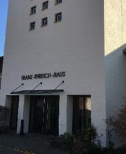 Eingang zum Franz-Ehrlich-Haus mit Überdachung und Büschen links und rechts.