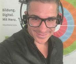 Mann mit dunklen haaren, schwarzer Jacke, Brille und Headset auf dem Kopf.