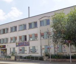 Bild vom Gebäude der Einrichtung. Helle Fassade mit hell-grünen Platten neben den Festern.