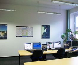 Seminarraum mit 3 Arbeitsplätzen jeweils mit 2 Bildschirmen, einem Bürostuhl, Tastatur, Maus und Headset. An der Wand Plakate und ein Wandkalender.