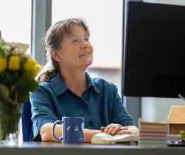 Eine Frau in blauer Bluse sitzt vor einem Monitor und schaut auf den Bildschirm.