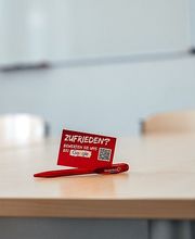 Beispiel Unterrichtsraum vor Ort mit Tisch, Stühlen und White Board an der Wand.