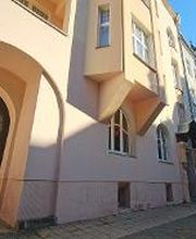 Eingangstor zum gelben Gebäude. Davor sind Fahrradständer und Parkplätze.