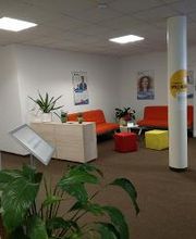 Gemütliche Lobby mit Sitzbereich bestehend aus 2 roten Sofas, und Sitzhocker. Werbeaufsteller, Plakate an der Wand und einige, grüne Zimmerpflanzen.