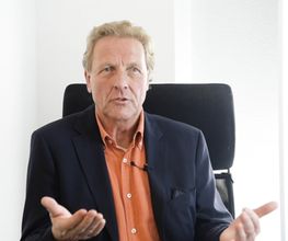 Ein Mann spricht in einem professionellen Umfeld vor der Kamera. Seine Gestik und Mimik vermitteln Offenheit, Kompetenz und Vertrauen.