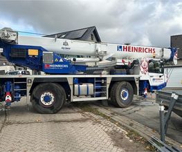 Mobilkran mit AS-BAU Aufkleber hebt Material für den Rohbau an einem Wohnhaus.