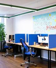 Ein Schulungsraum mit mehreren Arbeitsbereichen, die durch blaue Trennwände voneinander getrennt sind. Jeder Arbeitsplatz besteht aus 2 PC-Bildschirmen, Tastatur und Maus sowie Headset.