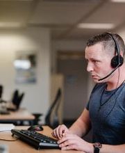 Ein Mann sitzt an einem PC-Arbeitsplatz und hat ein Headset auf dem Kopf