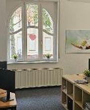 Schulungsraum mit mehreren Arbeitsplätzen mit jeweils 2 Bildschirmen, einem Bürostuhl, Tastatur, Maus und Headset. An den Wänden hängen Plakate und Bilder.