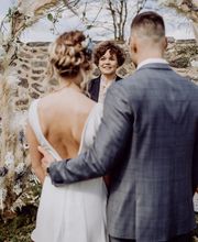 Eine Hochzeitszeremonie in der Natur: Ein Paar steht zwischen hohen Bäumen und nimmt an der freien Trauung teil.