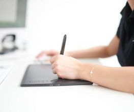 mediaService Bremen | Full-Stack Werbeagentur - Detailaufnahme einer Designerin bei der präzisen Arbeit mit einem Grafiktablett und digitalen Stift am Schreibtisch in einer modernen Designagentur.