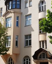 Gelbes Gebäude mit Vorsprung und Überdachter Eingangstür. Davor parkt ein Auto.