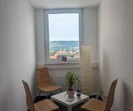 Ein kleiner Raum mit 3 Stühlen, Beistelltisch, Stehlampe und Fenster. Auf dem Tisch befindet sich eine kleine Topfpflanze.