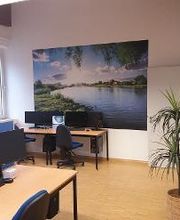 Ein Schulungsraum mit mehreren PC-Arbeitsplätzen. An der Wand hängt ein großes Bild eines Flusses.