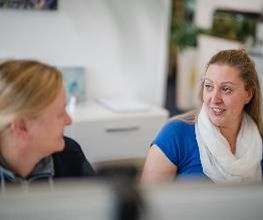 2 Frauen sitzen nebeneinander und schauen sich an.