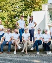 Team Region Bautzen-Görlitz, bestehend aus 9 Personen. Alle im weißen WBS GRUPPE T-Shirt am Brunnen vor einem Gebäude mit vielen großen Fenstern.