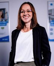 Portrait einer Mitarbeiterin mit hellbraunen Haaren und Brille, die freundlich in die Kamera lächelt.