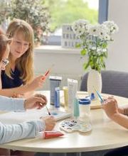 Hier sitzen drei Damen an einem Tisch in einem hellen, gemütlichen Raum und malen ein Bild.