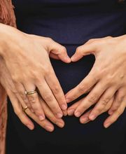 Kara Elizabeth Photography Detailaufnahme von Händen in Herzform über dem Bauch – Schwangerschaftsfotografie in München, die Vorfreude auf das Baby liebevoll dokumentiert.