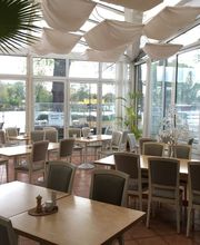 Großer, heller Aufenthaltsraum mit vielen Sitzmöglichkeiten. Viele Fenster und Blick nach draußen auf die Terrasse.