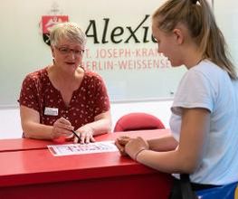 Empfang im Krankenhaus, Mitarbeiterin erklärt Patientin den Weg anhand des Lageplans