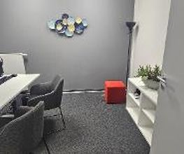 Arbeitsbereich mit 2 PC-Bildschirmen, Tastatur, Maus und Headset. Hellgraue Wände mit Dekoration. weißes Regal mit Topfpflanze.