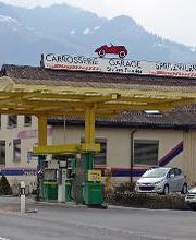 AGROLA Tankstelle in Benken. Geschwungene Glasüberdachung mit gelbem Metall. Zwei Tanksäulen. Im Hintergrund Gebäude mit Schild Carrosserie Garage Spritzwerk Schriftzug