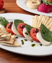 Caprese Appetizer: Thickly sliced buffalo mozzarella topped with roma tomatoes, fresh basil, kalamata olives, & homemade pesto