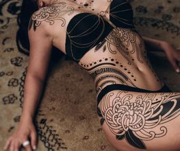 Ornamental Tattoo mit Chrysanthemen auf den Hüften. Symmetrisch vom Dekolleté bis auf die Oberschenkel. Blackwok und feminin